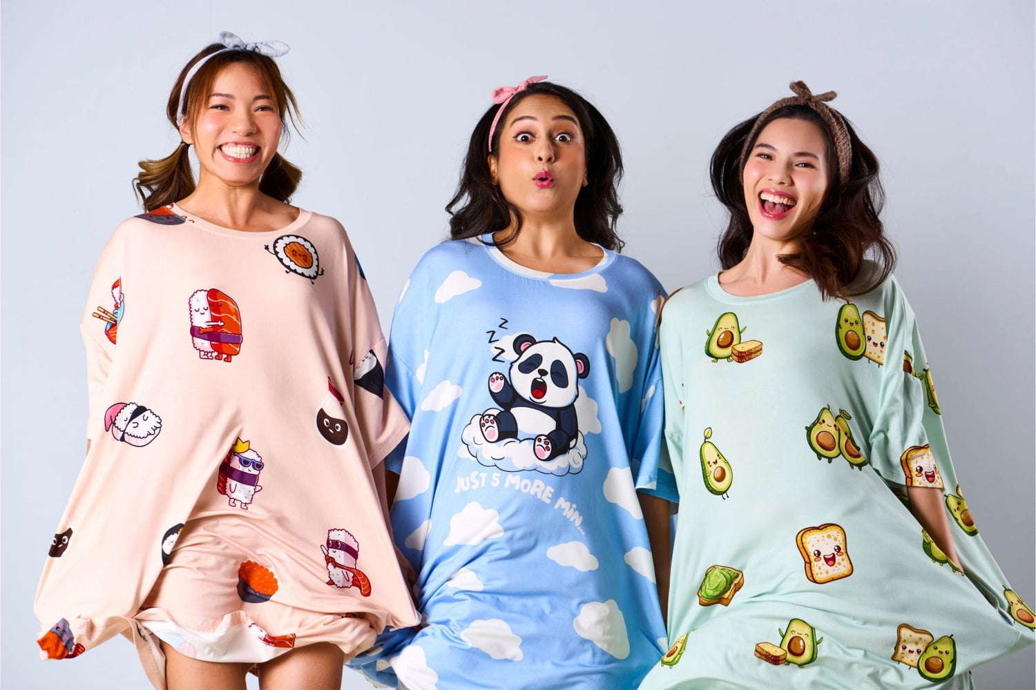 Three women wearing pajama sets with cartoon designs on a gray background having fun, jumping